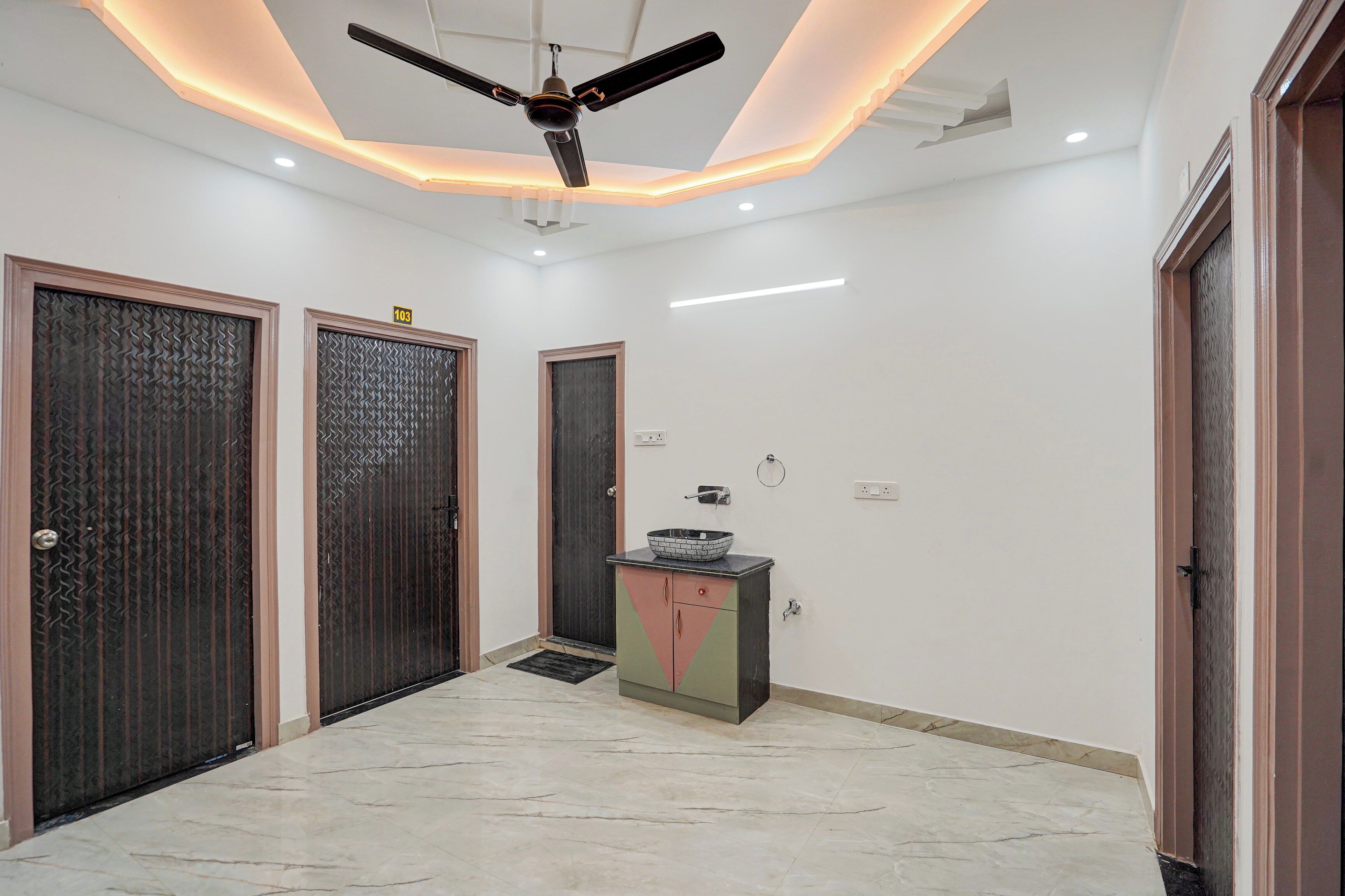 A hallway with three doors, a ceiling fan, recessed lighting, and a small cabinet with a bowl on top.