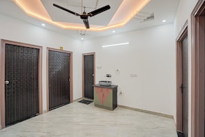 A hallway with three doors, a ceiling fan, recessed lighting, and a small cabinet with a bowl on top. - Hotel O Holiday Inn (Gorakhpur)