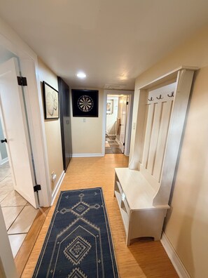 Un couloir avec un tapis à motifs, un jeu de fléchettes et un banc.