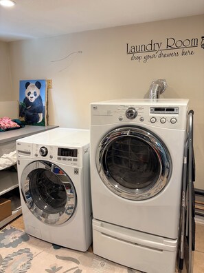 Une buanderie équipée de deux machines à laver à chargement frontal superposées, d’un sèche-linge fixé au mur et ornée d’un tableau représentant un panda.