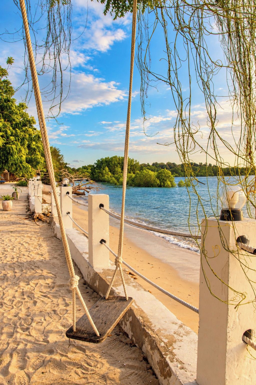 A sandy beach with a rope barrier, palm trees, and a body of water.