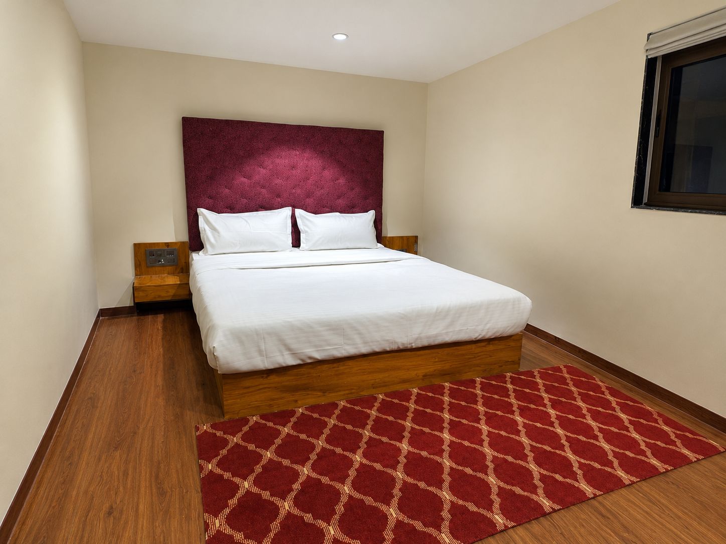 Ein Hotelzimmer mit einem großen Bett, einem roten Teppich mit Muster, Holzboden und einer cremefarbenen Wand.