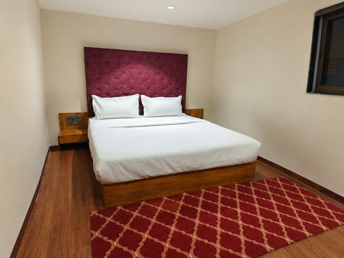 Ein Hotelzimmer mit einem großen Bett, einem roten Teppich mit Muster und einem hölzernen Kopfteil.