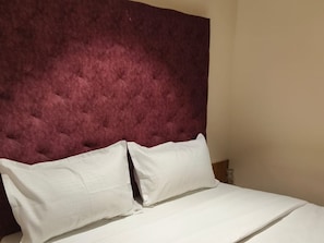 A bed with a tufted headboard and two pillows. - Hotel Bellora Suites (Rajkot)