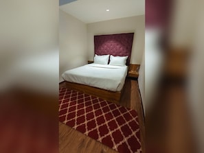 A hotel room with a bed, a red patterned rug, and a wooden floor. - Hotel Bellora Suites (Rajkot)