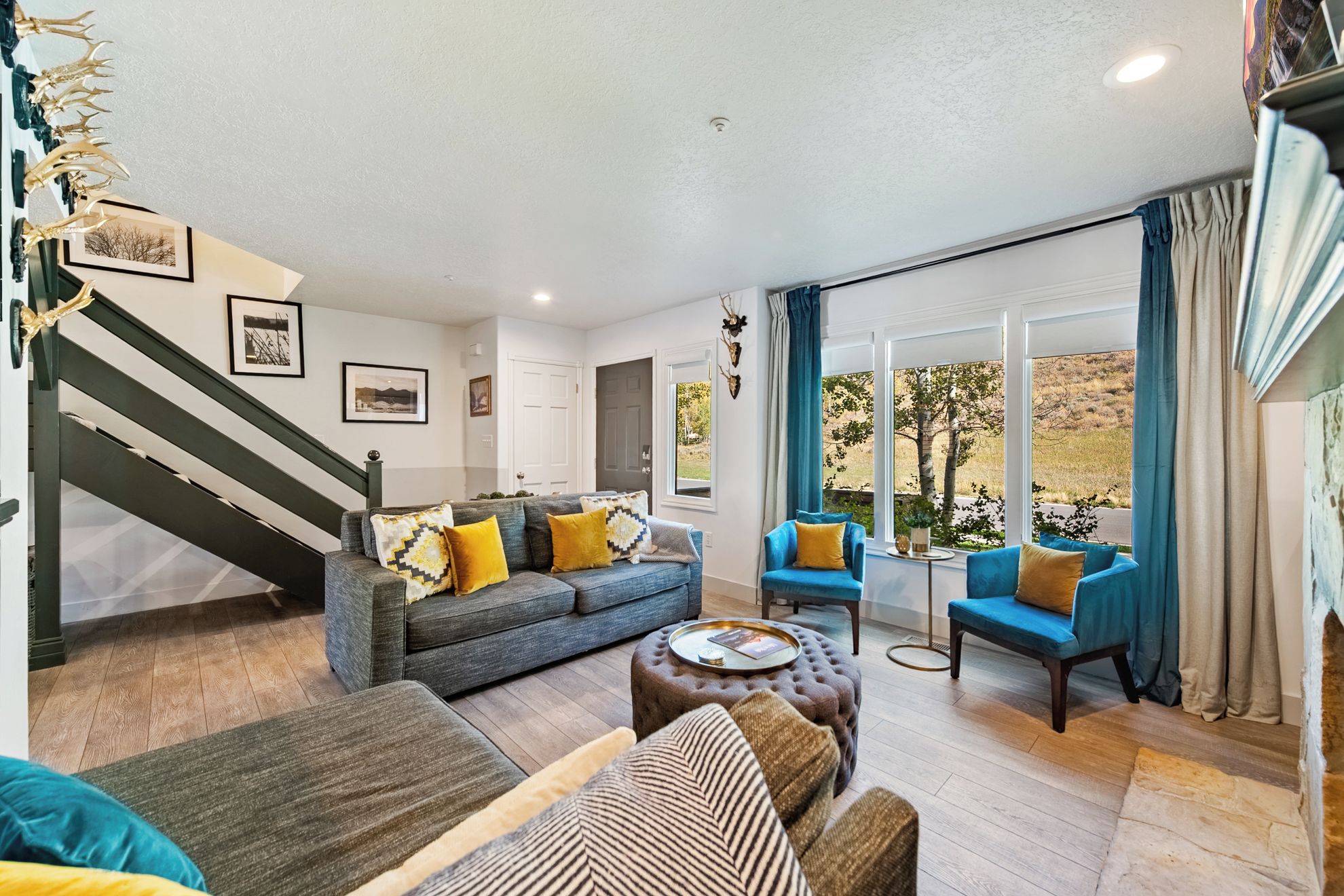 A spacious living room with a grey sofa, blue armchairs, and a coffee table. A staircase with a dark railing is visible on the left.
