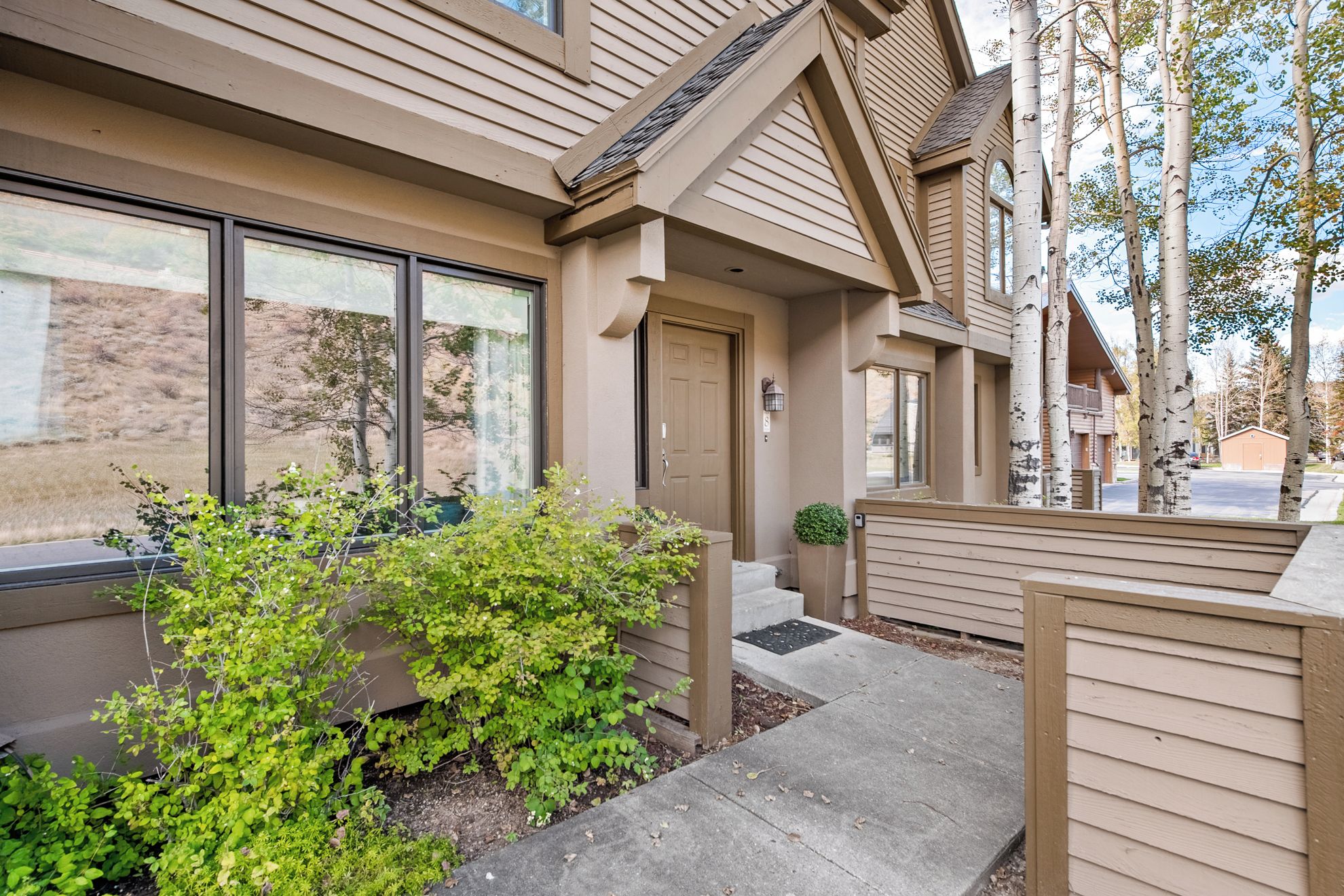A residential building with a front porch, large windows, and a small garden area.