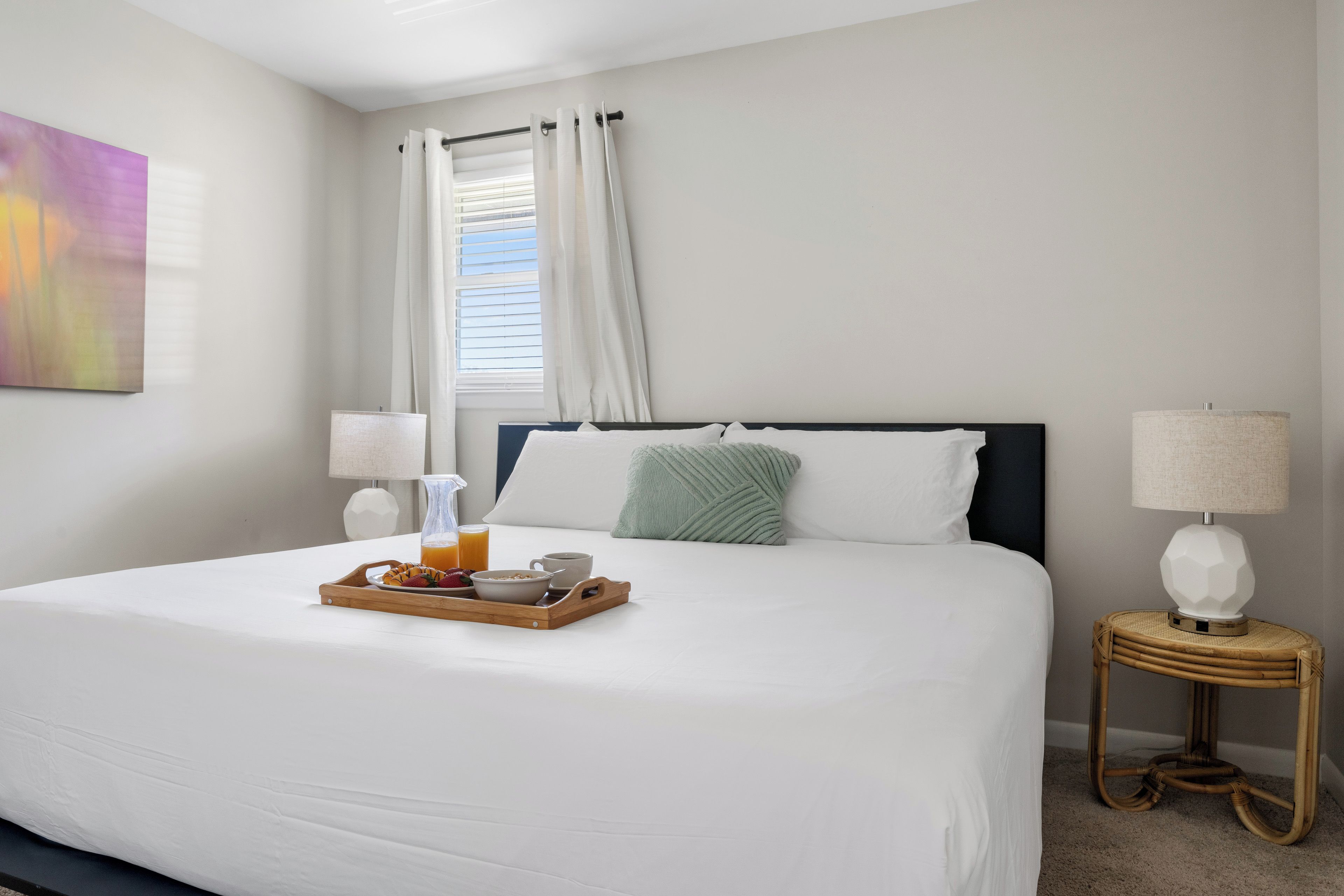 Une chambre d’hôtel avec un lit soigneusement fait, un plateau de petit-déjeuner, deux lampes de chevet et une fenêtre avec des rideaux.