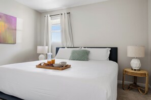 Een hotelkamer met een net opgemaakt bed, een dienblad met ontbijt, twee bedlampen en een raam met gordijnen.