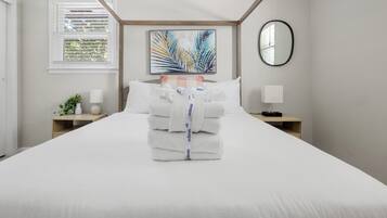 A neatly made bed with folded towels and a decorative palm leaf painting above it.