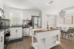 Een moderne keuken met witte kastjes, een centraal eiland en een eethoek met een kroonluchter.