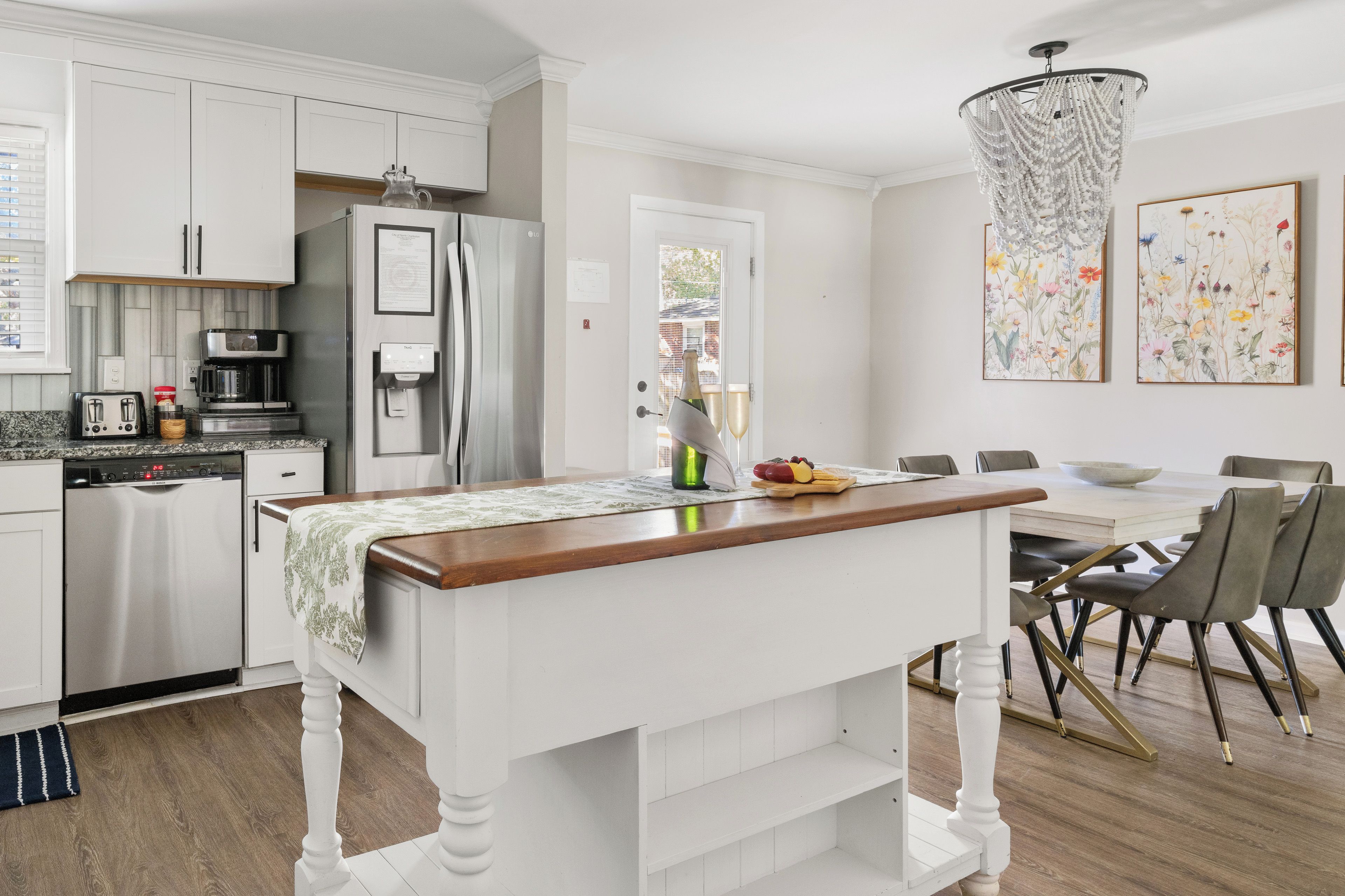 A modern kitchen with white cabinetry, a stainless steel refrigerator, a coffee maker, and a dining area with a table and chairs.