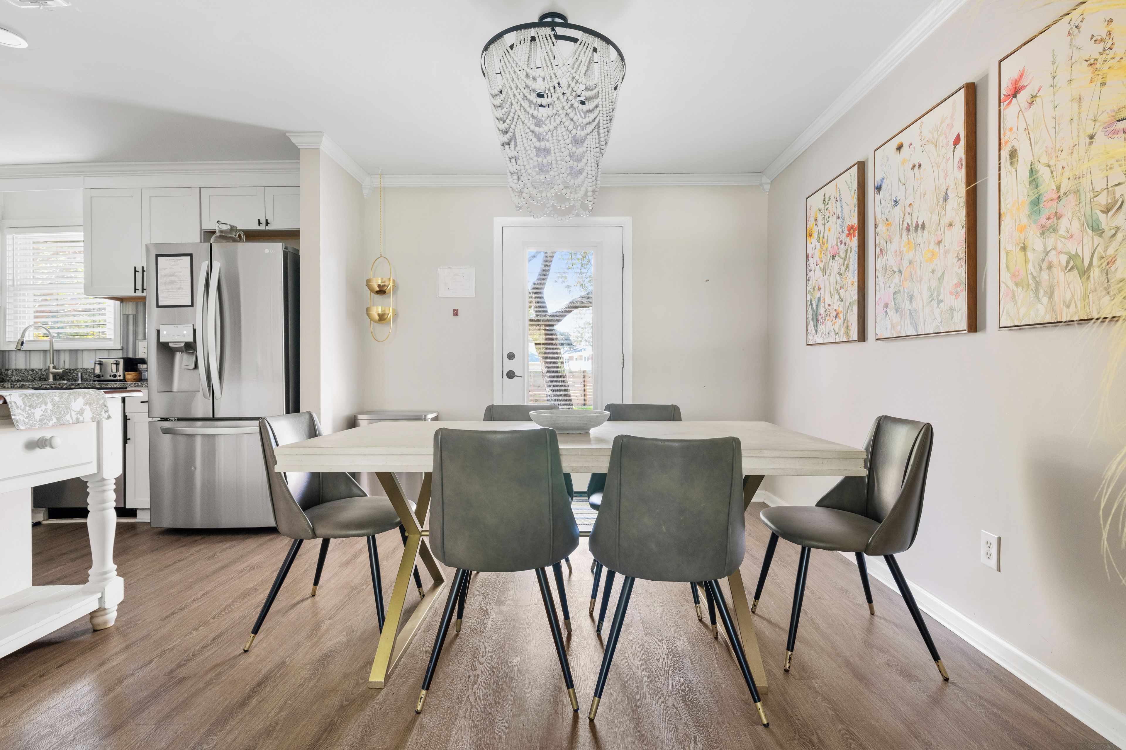 A modern kitchen with a stainless steel refrigerator, a dining table with chairs, and a chandelier.