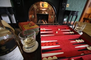 A mahjong table with tiles and a bottle of alcohol, a glass, and a fireplace in the background. - Isla Bank House (Keith)