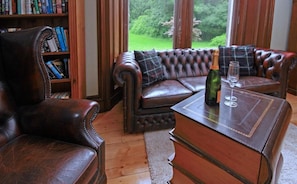 A leather sofa with a plaid cushion, a wooden coffee table with a bottle and glass, and a bookshelf filled with books. - Isla Bank House (Keith)