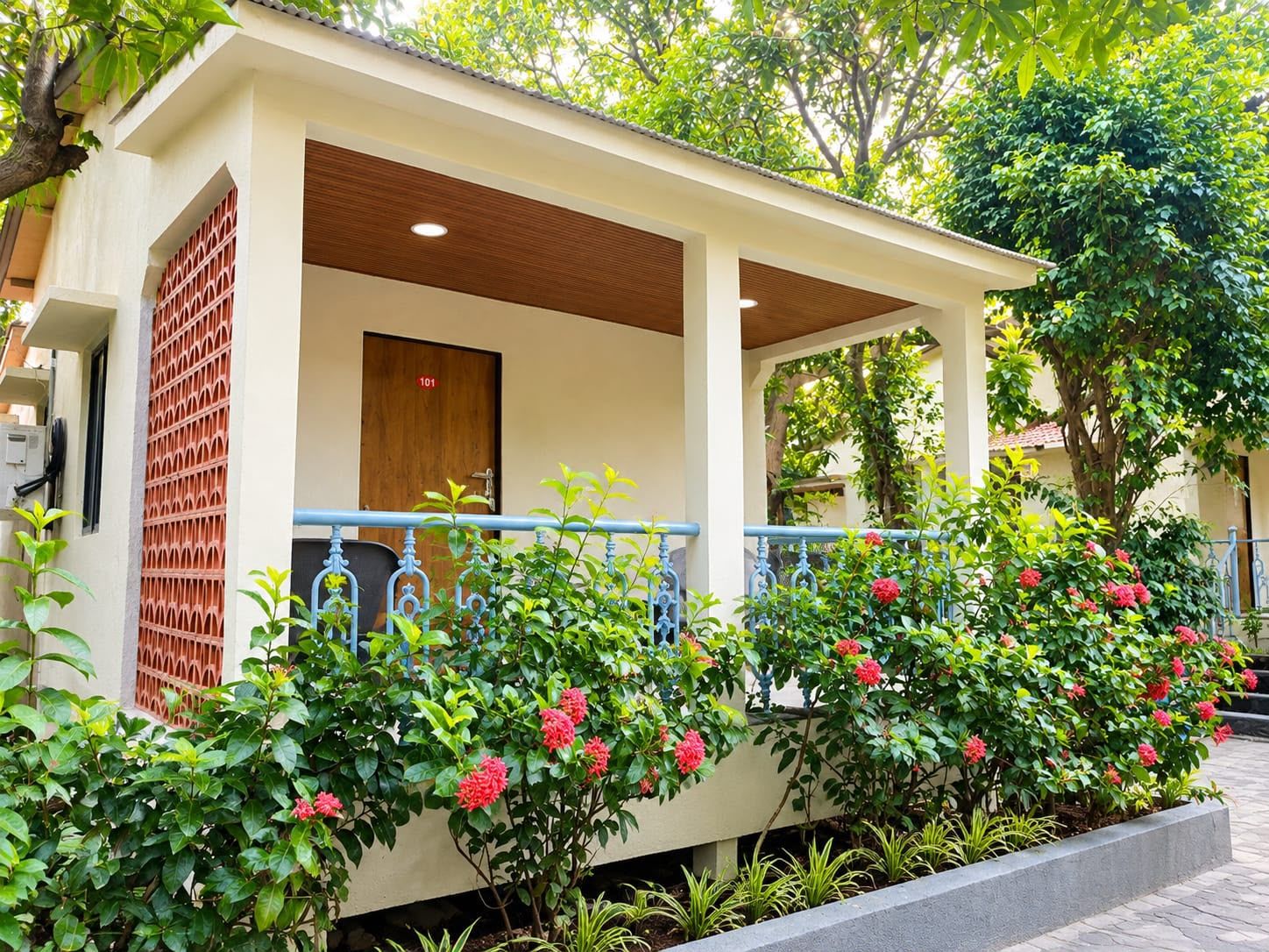 A building with a covered porch, a door with a number, and a garden with flowering plants.