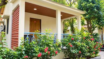 A building with a covered porch, a door with a number, and a garden with flowering plants.