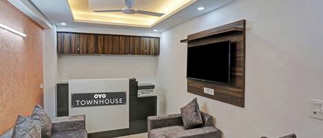 Un espace d’accueil avec une enseigne indiquant « OYO TOWNHOUSE », un ventilateur de plafond et un téléviseur à écran plat fixé au mur.