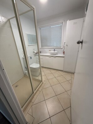 Ett badrum med en dusch som är avskärmad med glasväggar, en toalett och ett handfat med ett fönster ovanför.