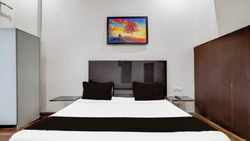 A hotel room with a bed, two pillows, a nightstand, a painting on the wall, and a wooden wardrobe.