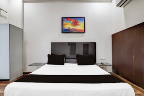 Habitación de hotel con cama, dos almohadas, mesita de noche, un cuadro en la pared y un armario de madera.