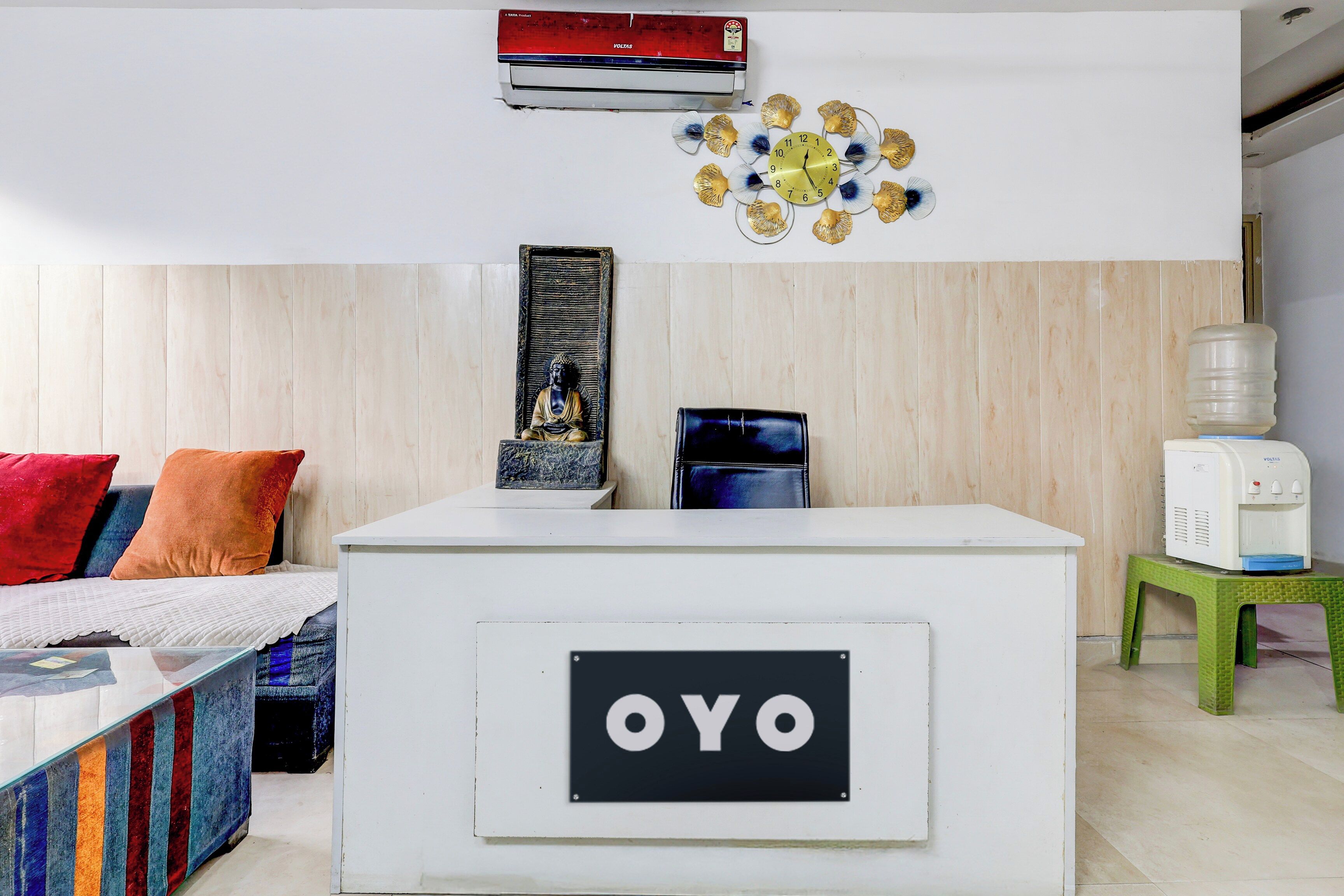 A room with a reception desk labeled 'OYO,' a water dispenser, a clock, and a Buddha statue.