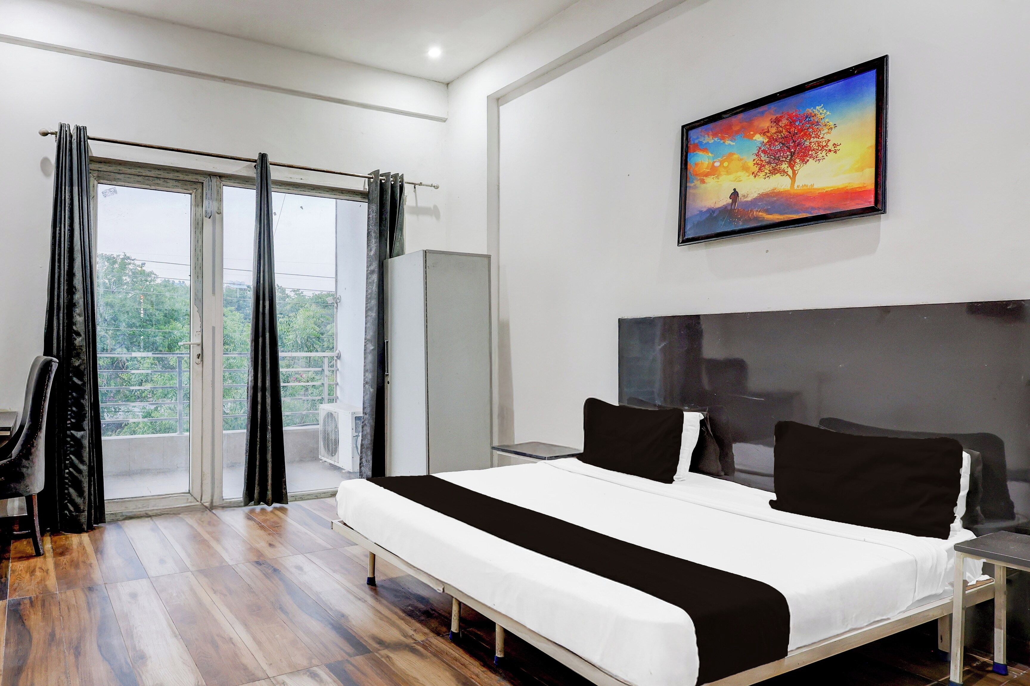 A bedroom with a bed, a painting, a chair, and a view through the window.