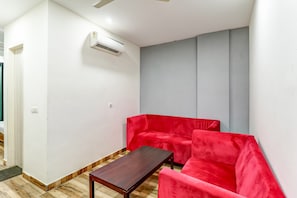Et værelse med en rød sofa, et træbord og en hvid aircondition installeret på væggen.