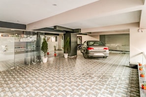 A parking garage with a car parked in the middle, potted plants, and a glass wall on one side. - Hotel O The Rise (Gurgaon)