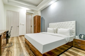 A hotel room with a large bed, wooden flooring, a wardrobe, a desk with a chair, and a bedside table with a kettle. - Hotel O The Rise (Gurgaon)