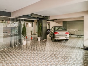 A parking garage with a parked car and potted plants. - Hotel O The Rise (Gurgaon)