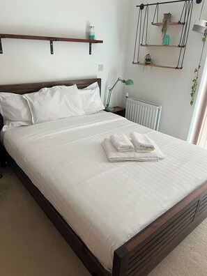 A neatly made bed with white linens, a bedside lamp, and a radiator. - Safe & Private London Apartment, Great Transport Links, Zone 2 (London)