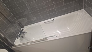 Una bañera blanca con un solo grifo y un cabezal de ducha manual, frente a una pared con azulejos.