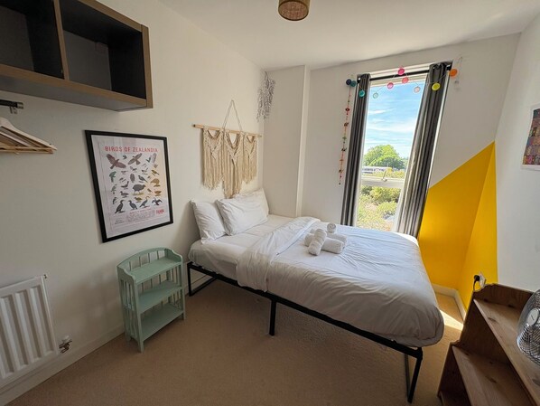 A bedroom with a bed, a framed poster, a macrame wall hanging, a window with curtains, and a radiator. - Safe & Private London Apartment, Great Transport Links, Zone 2 (London)
