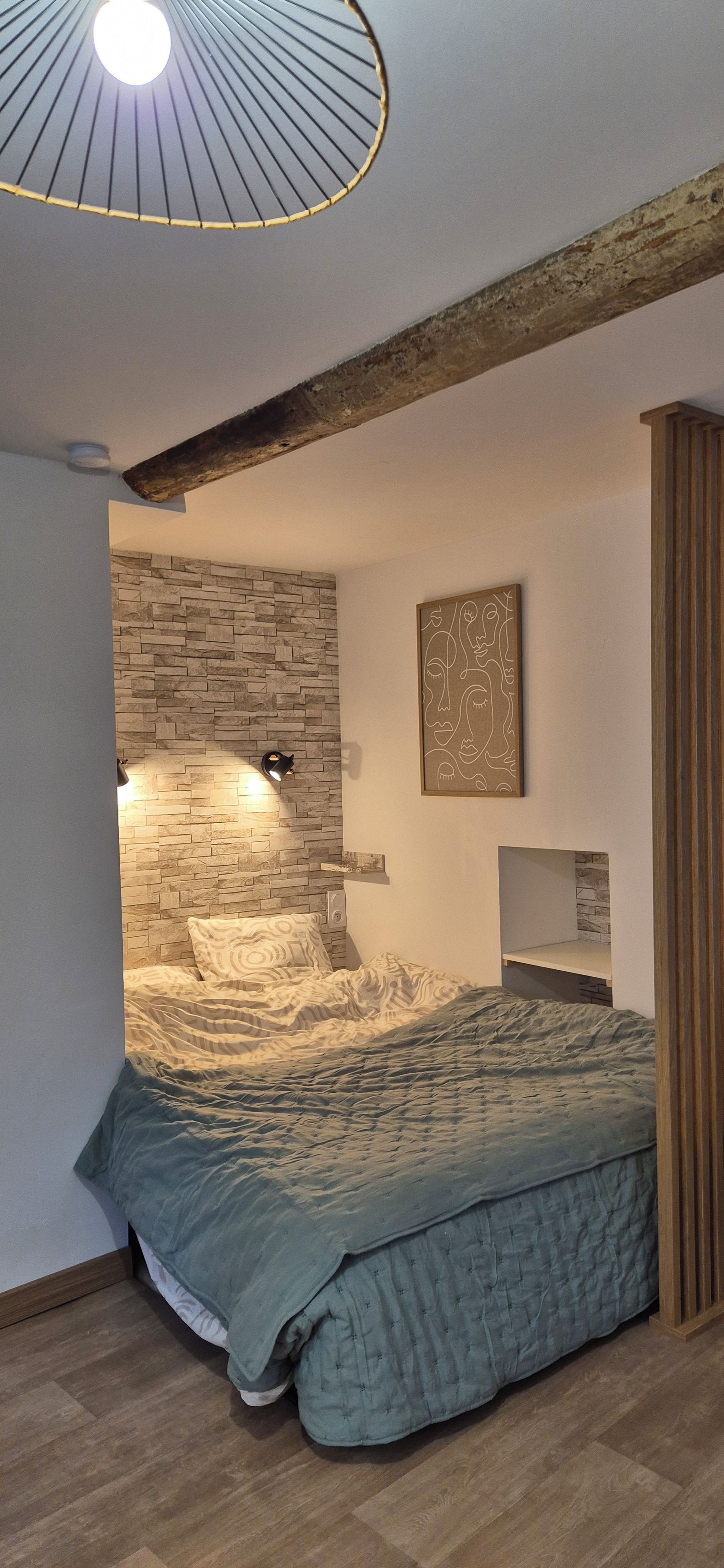 Ein Schlafzimmer mit einer Steinsandsteinwand, einem Bett mit gemustertem Überwurf, einer Deckenleuchte und einem Wandbild.