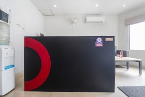 Un salón de conferencias con un separador grande de color negro y rojo, un dispensador de agua, un equipo de aire acondicionado y un ventanal con vistas.