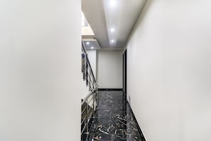 A corridor with a marble floor, metal railing, and a staircase leading to an upper level. - Hotel O Metro suites (Gurugram)