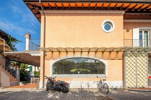 A building with a large arched window, a motorcycle parked in front, and a bicycle rack to the right. - New Listing (Forte dei Marmi)