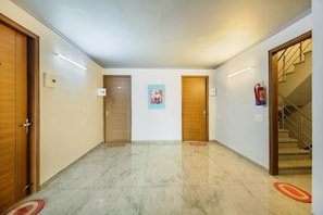 A hallway with two wooden doors, a fire extinguisher, and a staircase. - Hotel O by OYO VIJAYA RESIDENCY (Gurgaon)