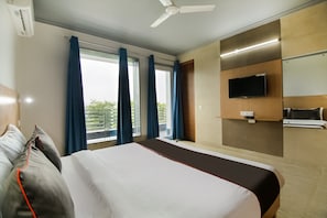 Et hotelværelse med en seng, et fjernsyn ophængt på væggen og et vindue med gardiner.