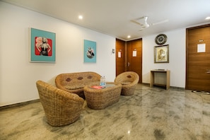 A lobby with wicker furniture, a clock, and framed artwork on the walls. - Hotel O by OYO VIJAYA RESIDENCY (Gurgaon)