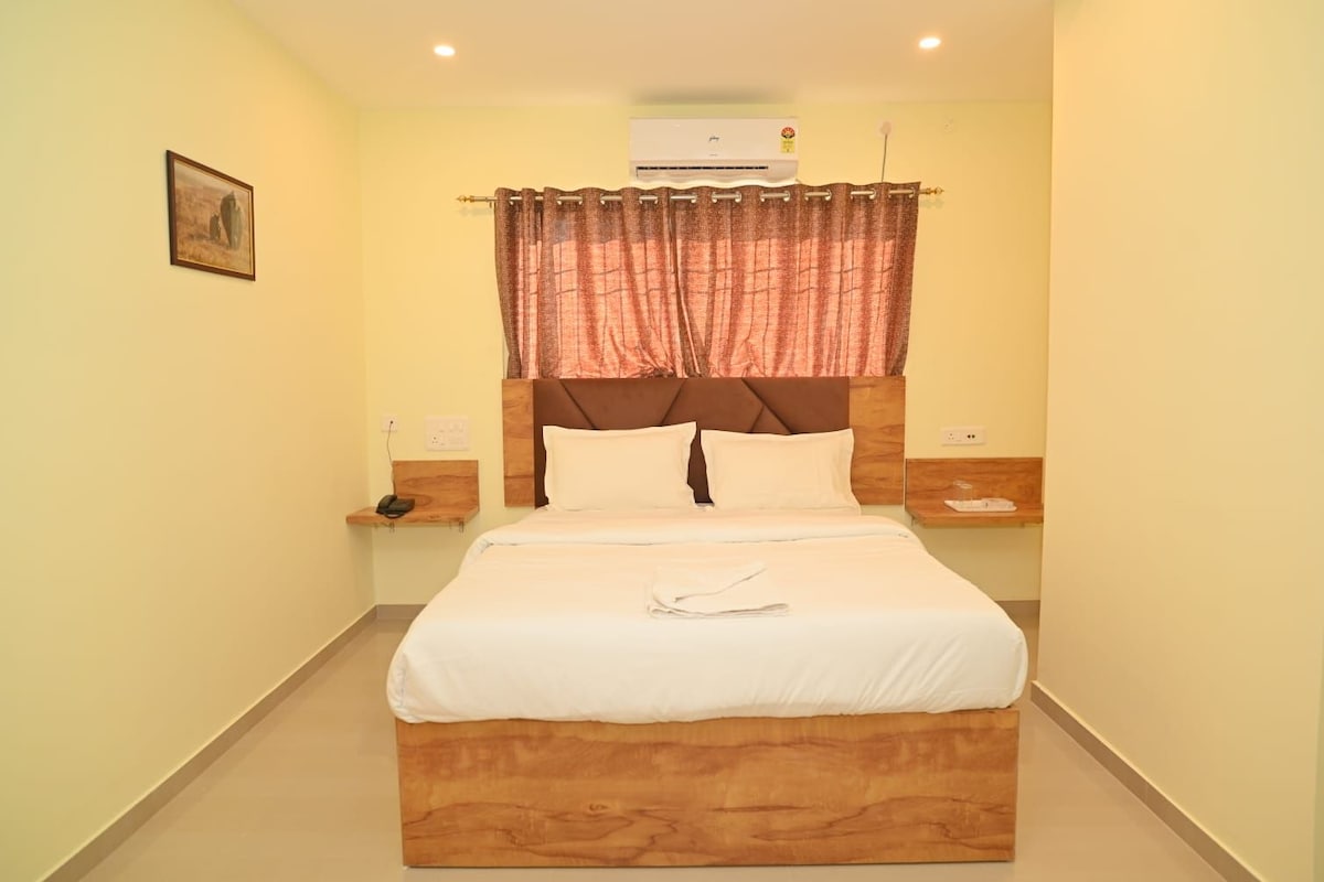 A hotel room with a bed, a nightstand, a wall-mounted air conditioner, and a painting on the wall.