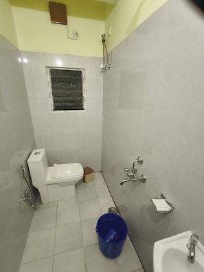 A small, tiled bathroom with a toilet, a shower, and a sink. - Vanveera Grand (Guwahati)