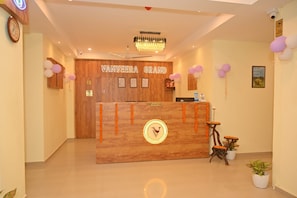 A reception desk with a wooden finish, a chandelier above, and a reception sign. - Vanveera Grand (Guwahati)