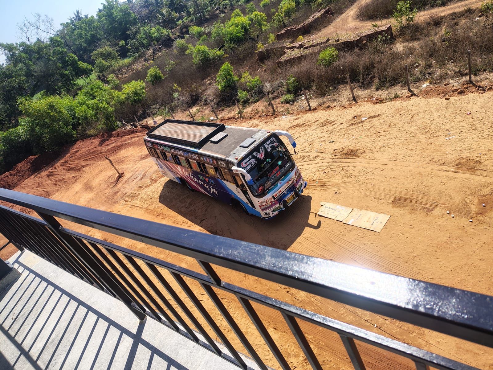 A bus parked on a dirt road with a metal railing in the foreground.
