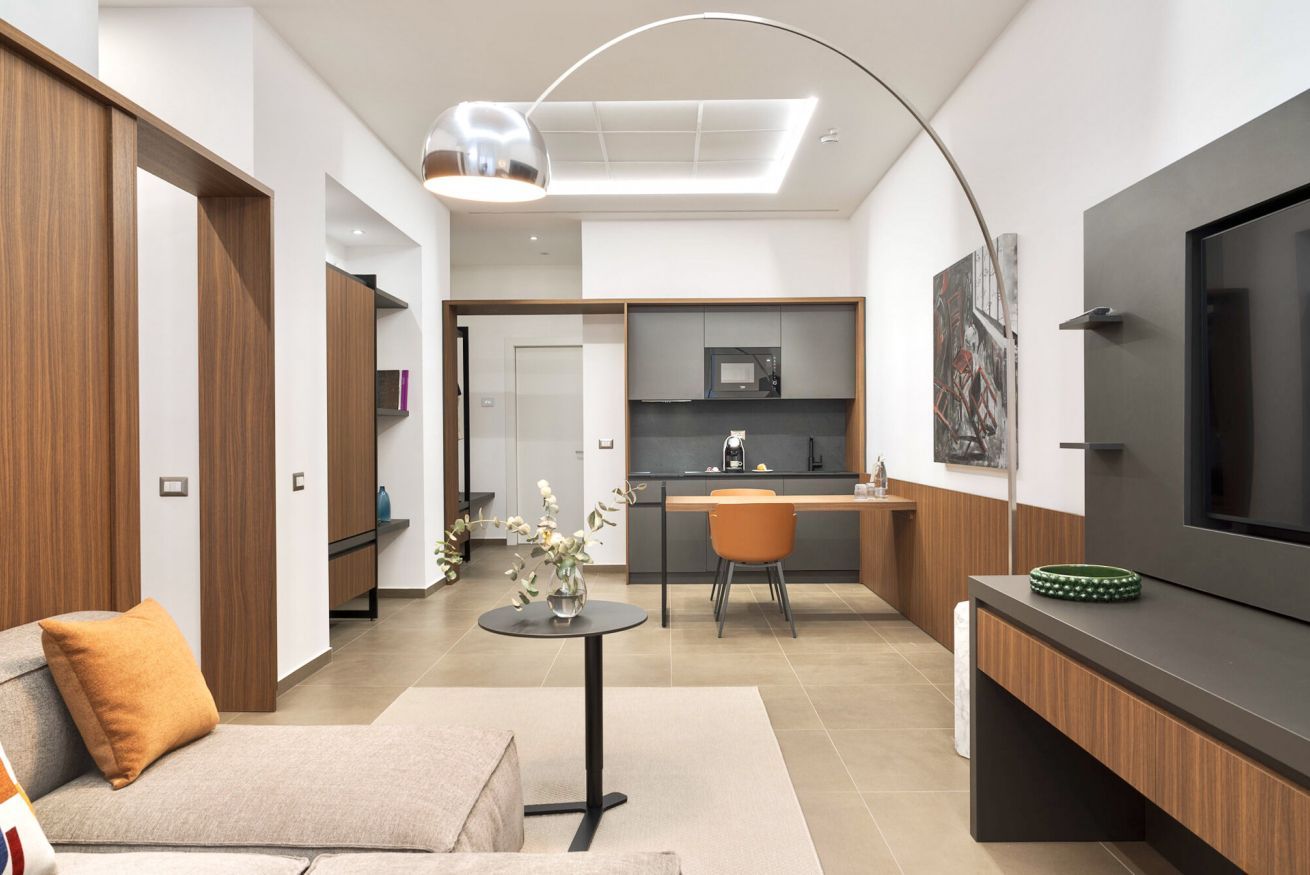 A modern living room with a sofa, a coffee table, and a TV. There's a kitchen area with a microwave and a dining table.