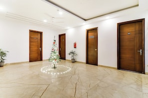 A hotel lobby with marble flooring, wooden doors, and a small Christmas tree with lights. - Hotel O Pink Stays (Gurugram)