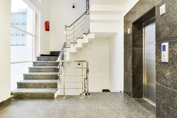A staircase with a metal handrail leading to an elevator. - Hotel O Pink Stays (Gurugram)
