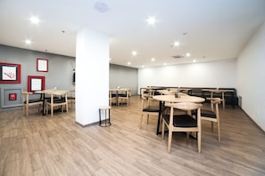 A spacious room with multiple tables and chairs, a white pillar, and framed items on the wall. - Hotel O Elite Stayz (Gurgaon)