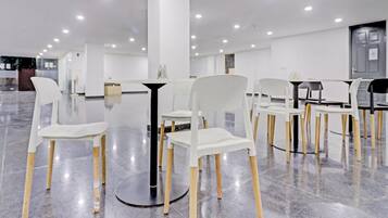 A modern interior with white chairs and tables arranged around a central column, a polished marble floor, and recessed ceiling lighting.